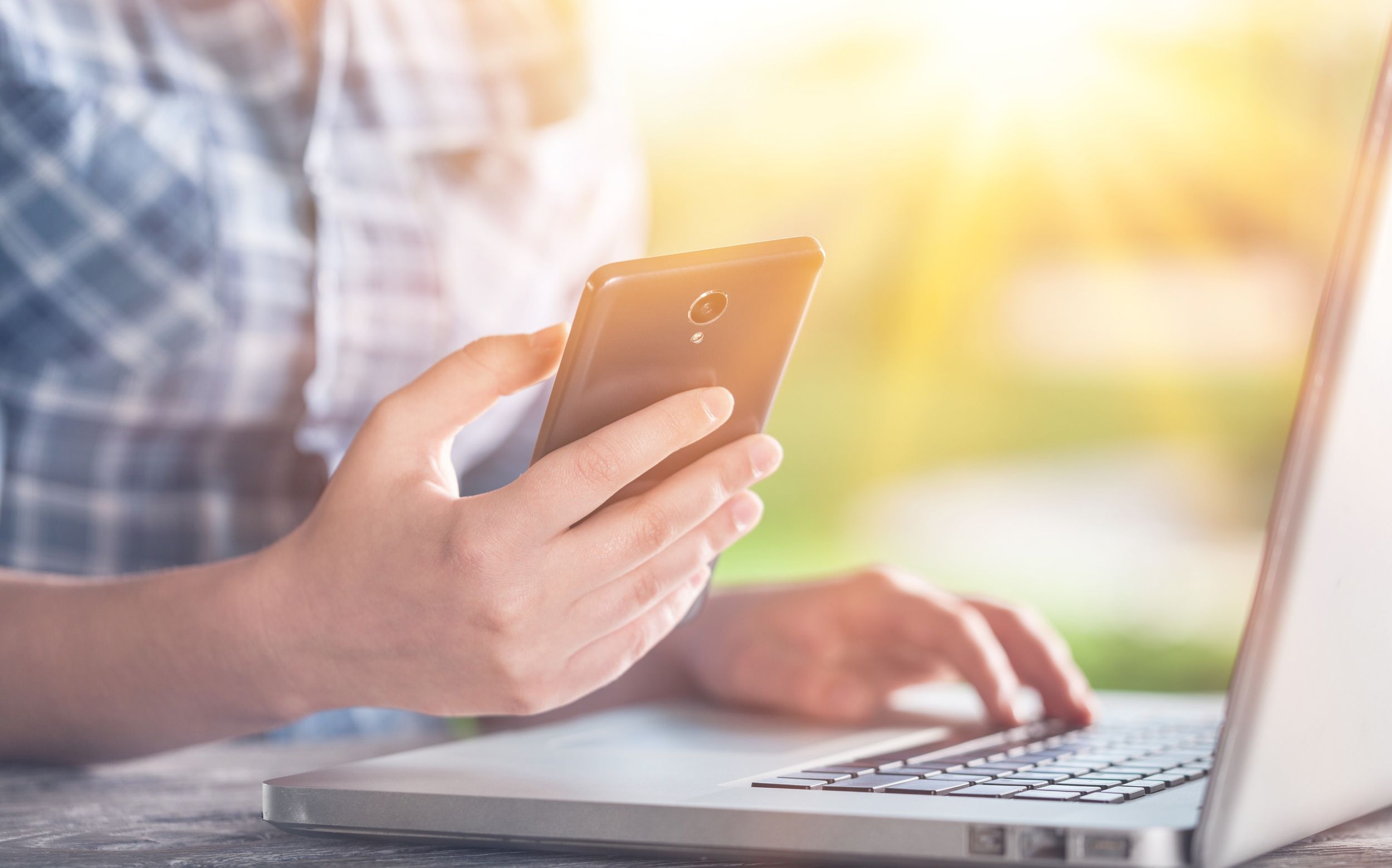 Person using a smartphone while typing on a laptop