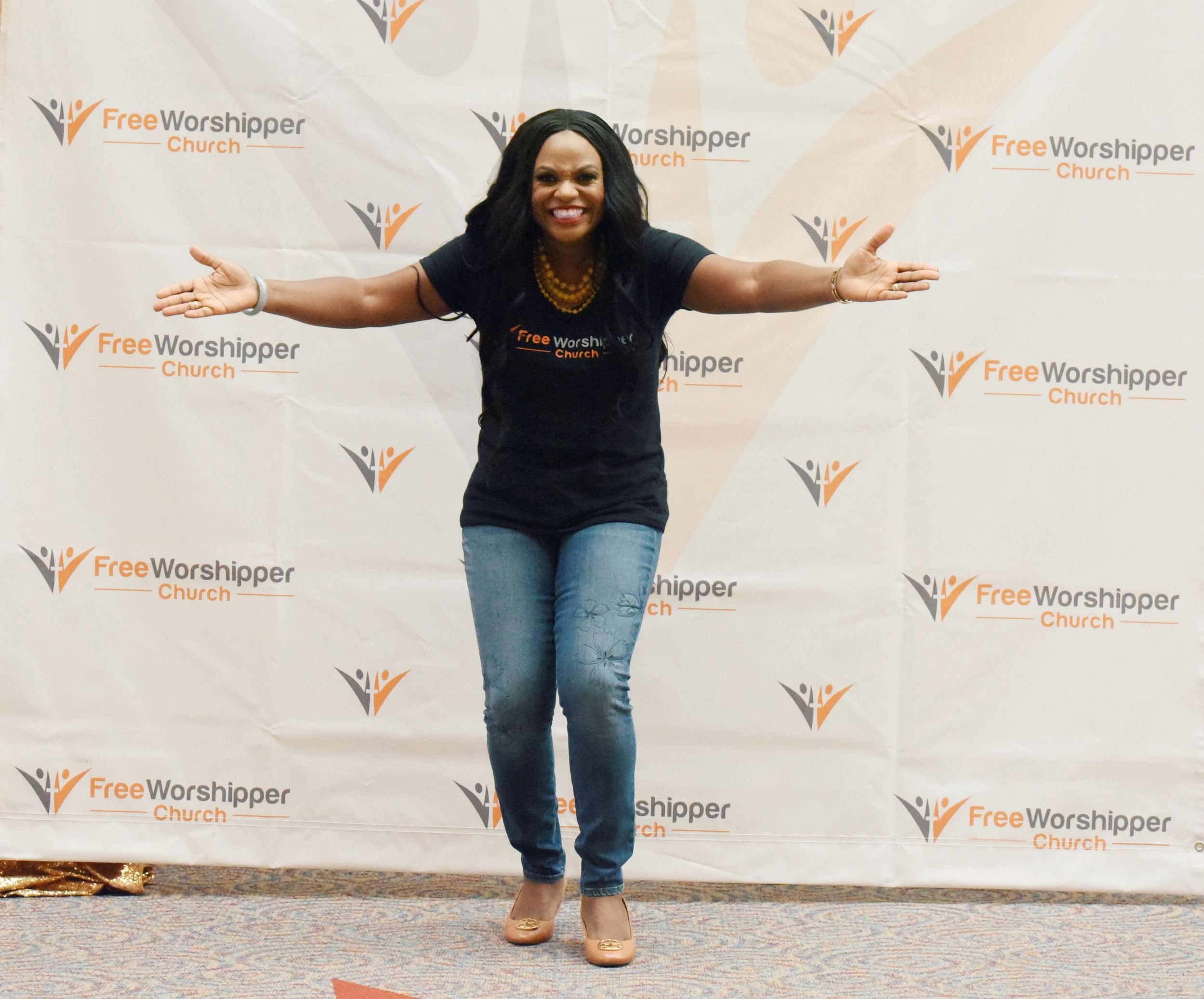 Woman smiling with open arms in front of a Free Worshipper Church backdrop