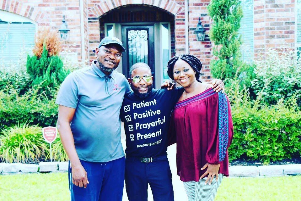 Three church members posing outside together in front of a brick home