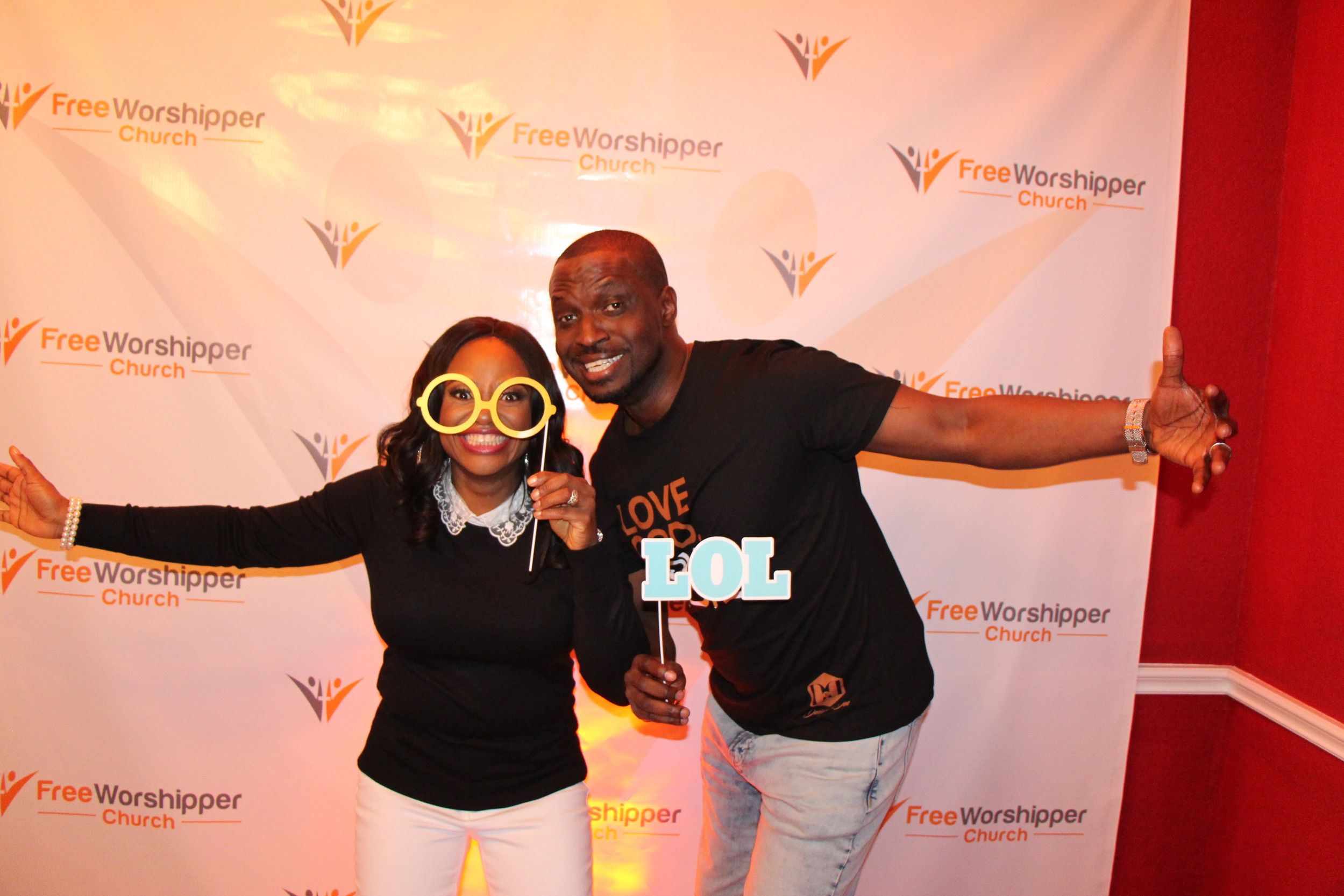 Two church guests posing with fun photo props in front of a Free Worshipper Church backdrop