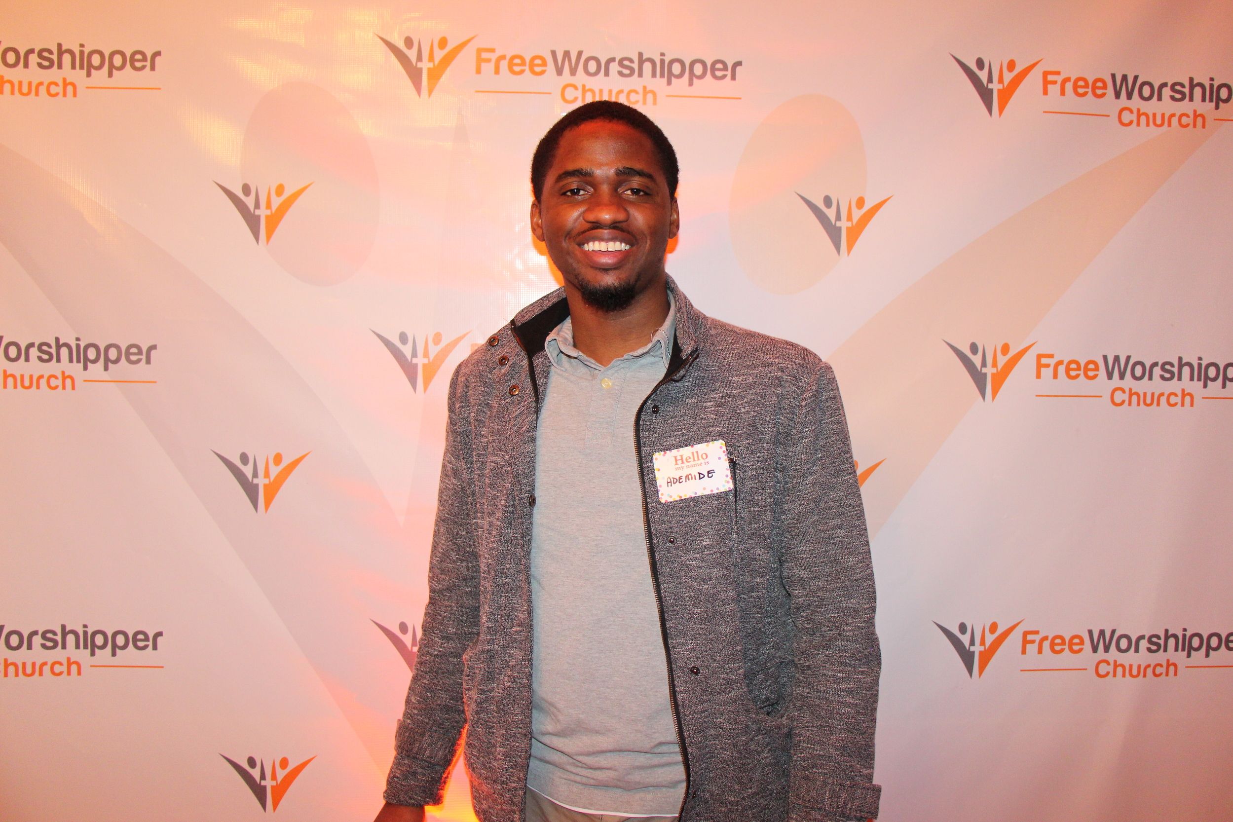 Smiling church guest standing in front of the Free Worshipper Church backdrop