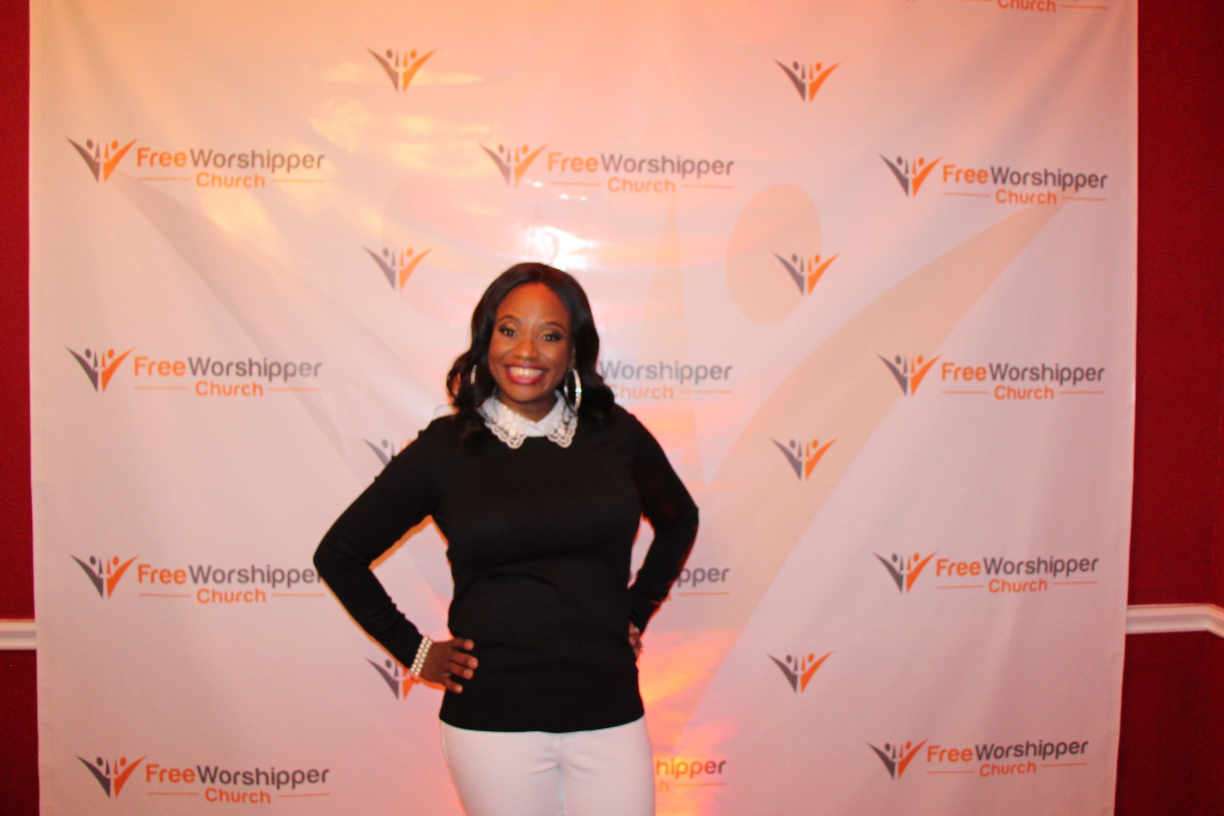 Woman smiling in front of the Free Worshipper Church event backdrop