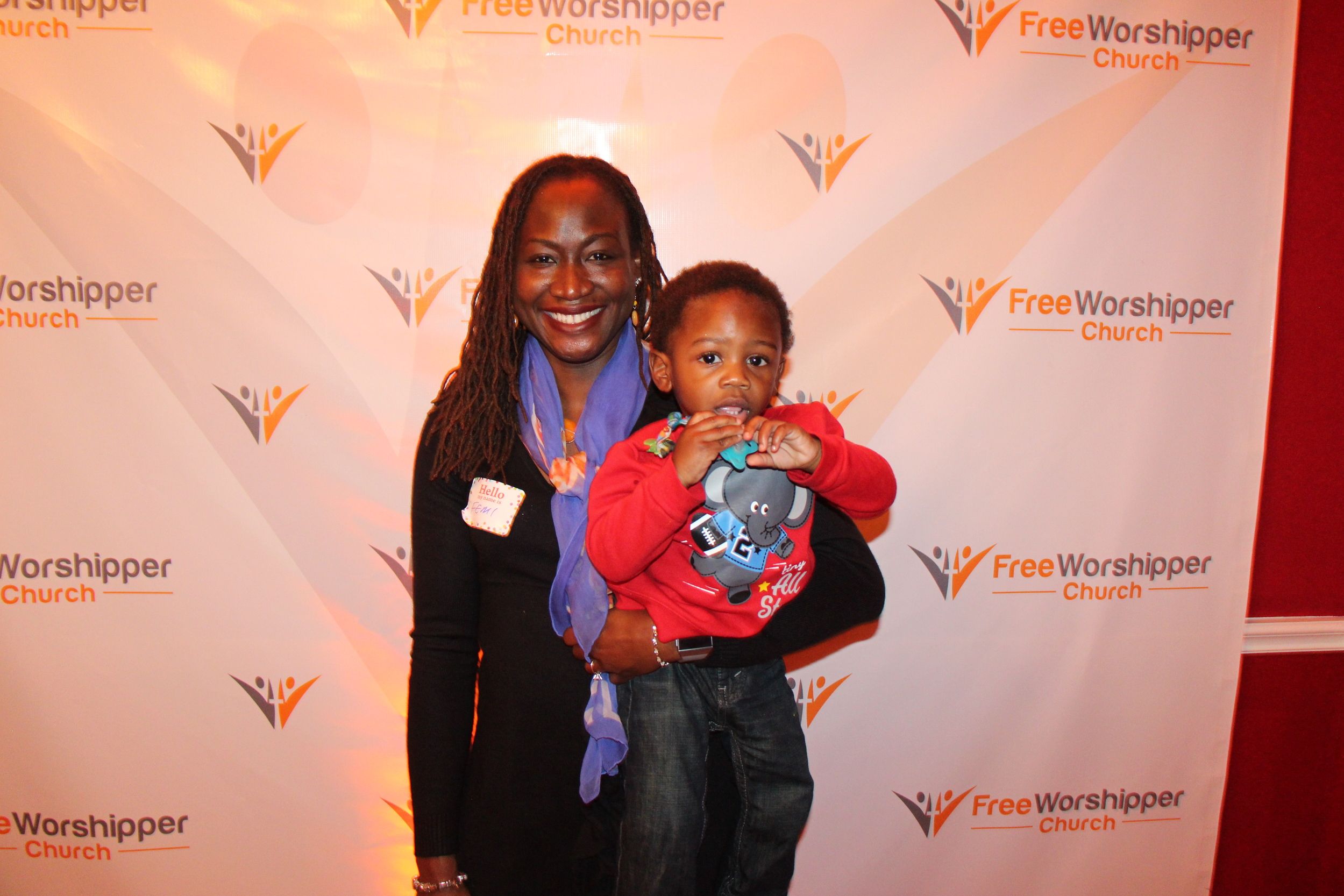 Woman holding a child in front of a Free Worshipper Church event backdrop