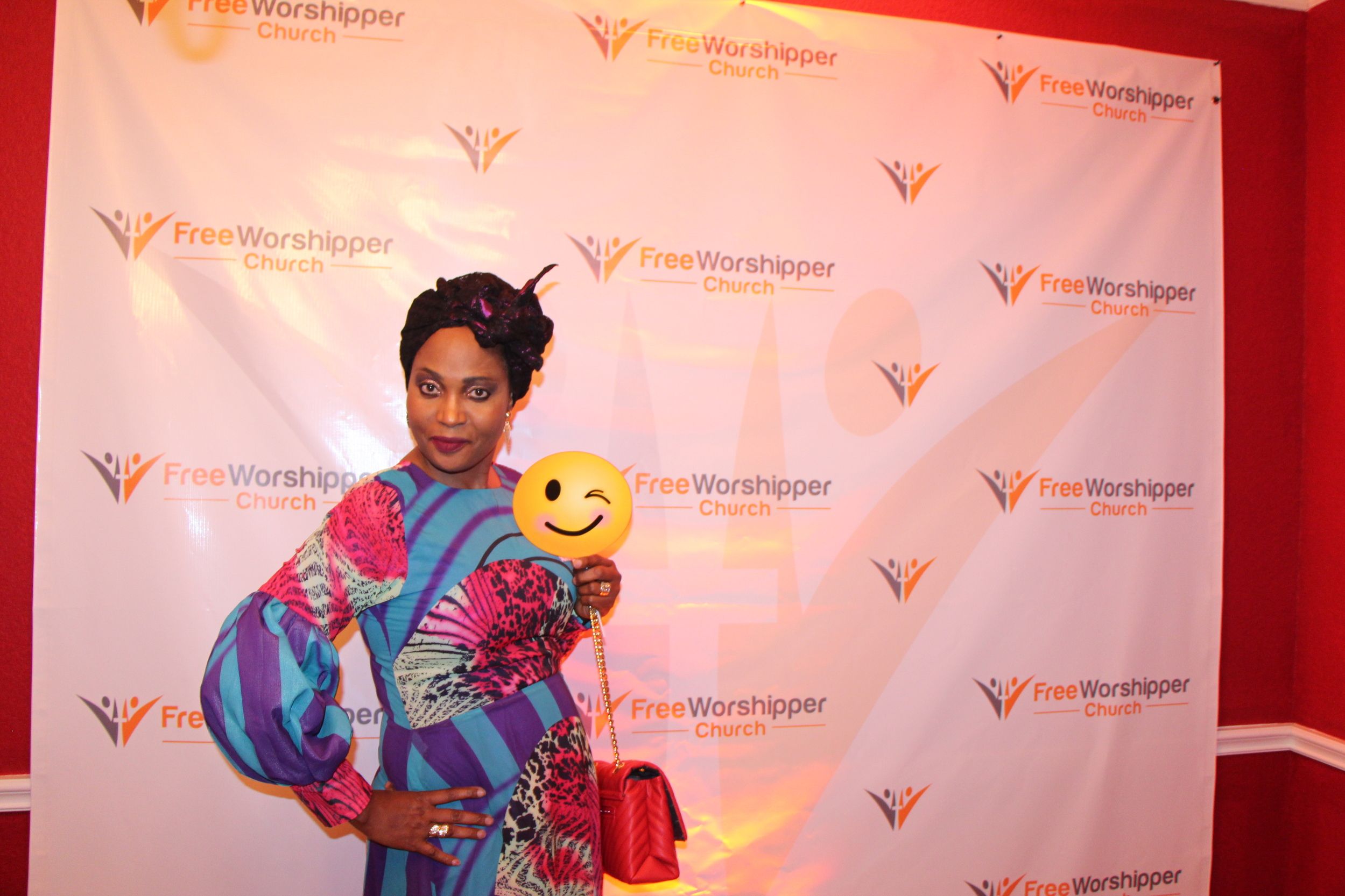 Woman posing with a smiley-face prop in front of the Free Worshipper Church backdrop