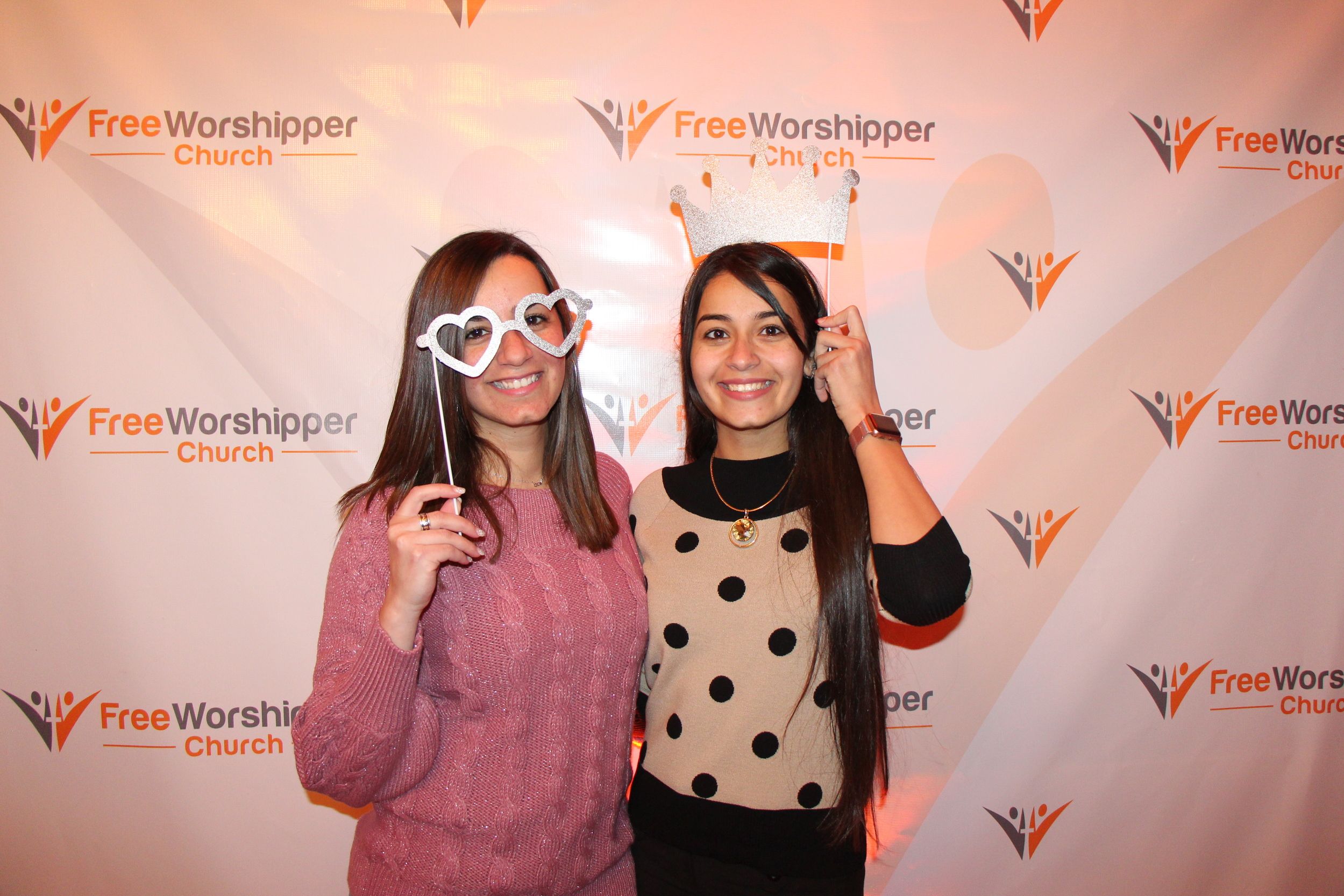 Two smiling women posing with heart-shaped glasses at a church meet and greet