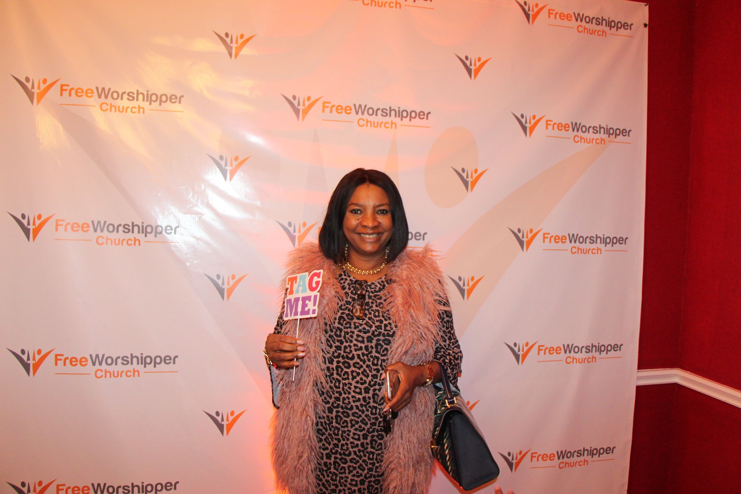Church guest holding a Tag Me sign at the Free Worshipper Church backdrop