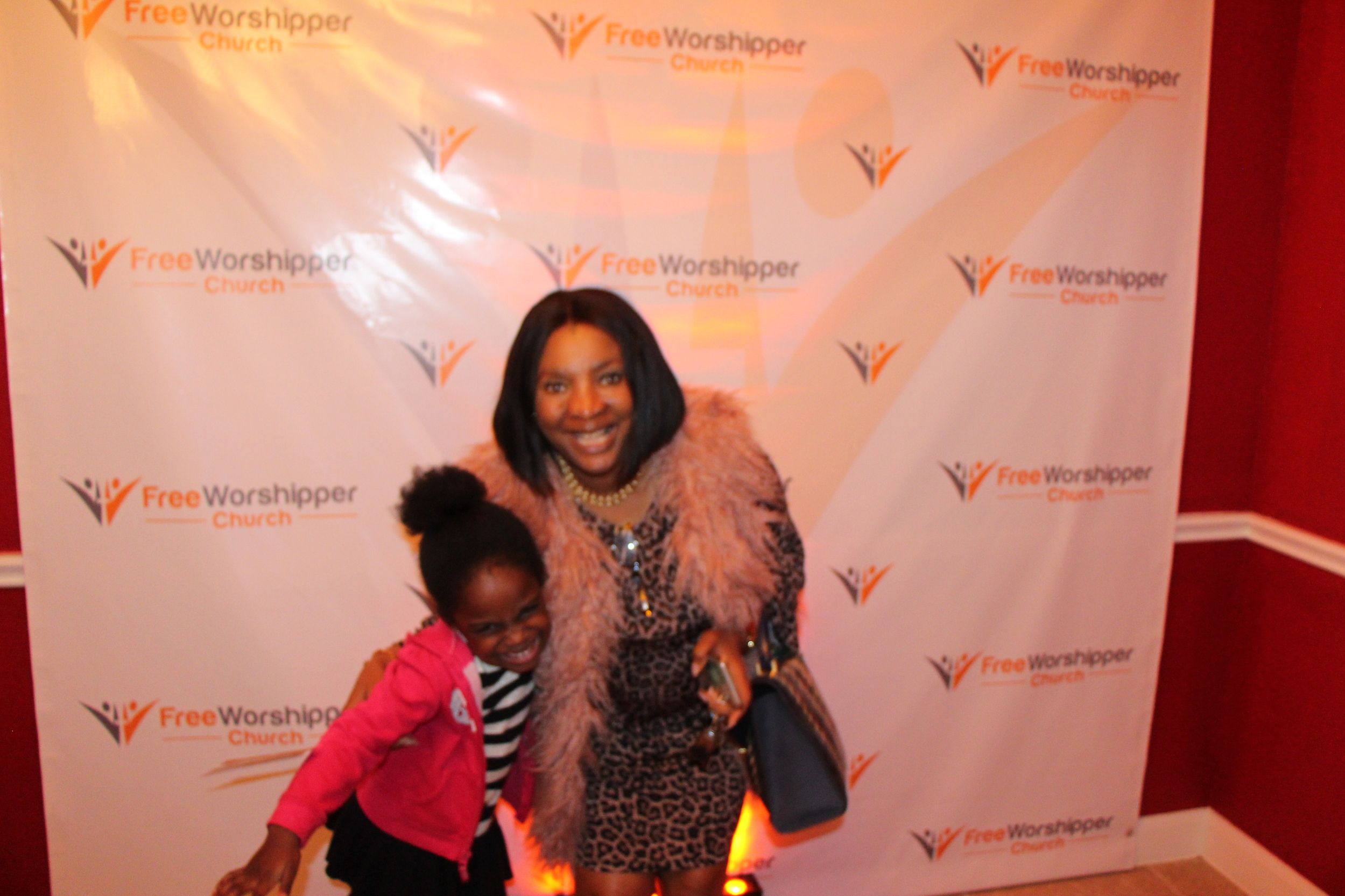 Two guests posing together in front of the Free Worshipper Church backdrop